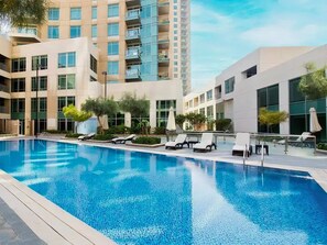 A modern hotel with a swimming pool, lounge chairs, and a high-rise building in the background.