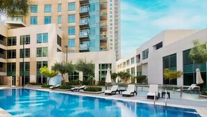 A modern hotel with a swimming pool, lounge chairs, and a high-rise building in the background. - Spacious 2BR in Downtown  | High Floor | 8 Guests (Dubai)