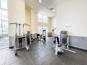 Ein Fitnessstudio mit verschiedenen Trainingsgeräten, großen Fenstern und einem gefliesten Boden.