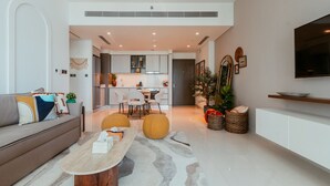 A modern living room with a sofa, coffee table, and a dining area with chairs and a table. - Oceanfront Escape: Stylish 1 BR  in Beachfront (Dubai)