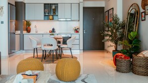 A modern kitchen with white cabinets, a dining area with a round table and chairs, and a living area with a sofa and decorative pillows. - Oceanfront Escape: Stylish 1 BR  in Beachfront (Dubai)