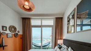 A hotel room with a large bed, a view of the sea, and a hammock outside the window. - Oceanfront Escape: Stylish 1 BR  in Beachfront (Dubai)