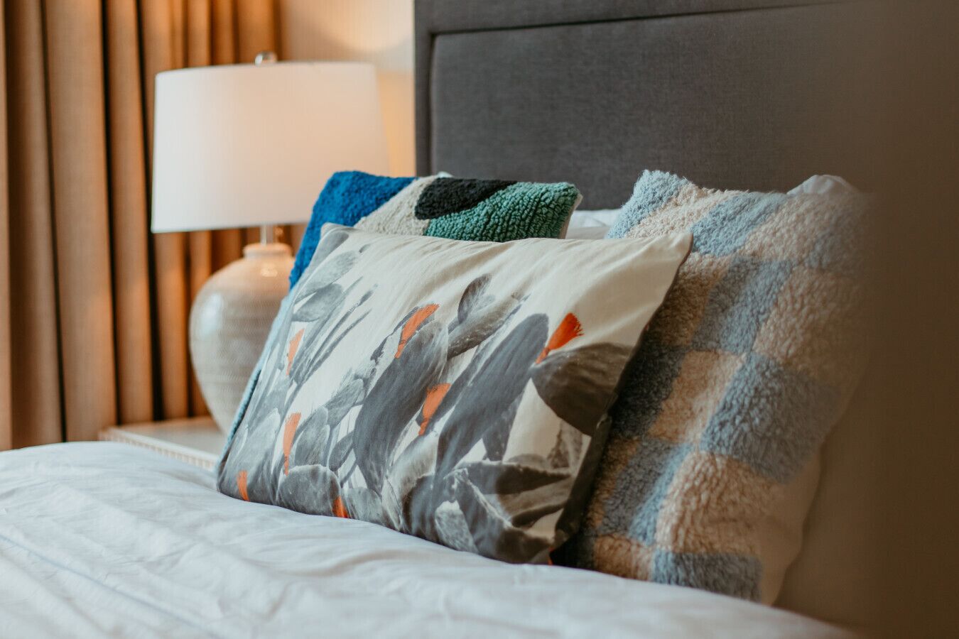 A neatly made bed with a white comforter and multiple pillows, including a patterned one.