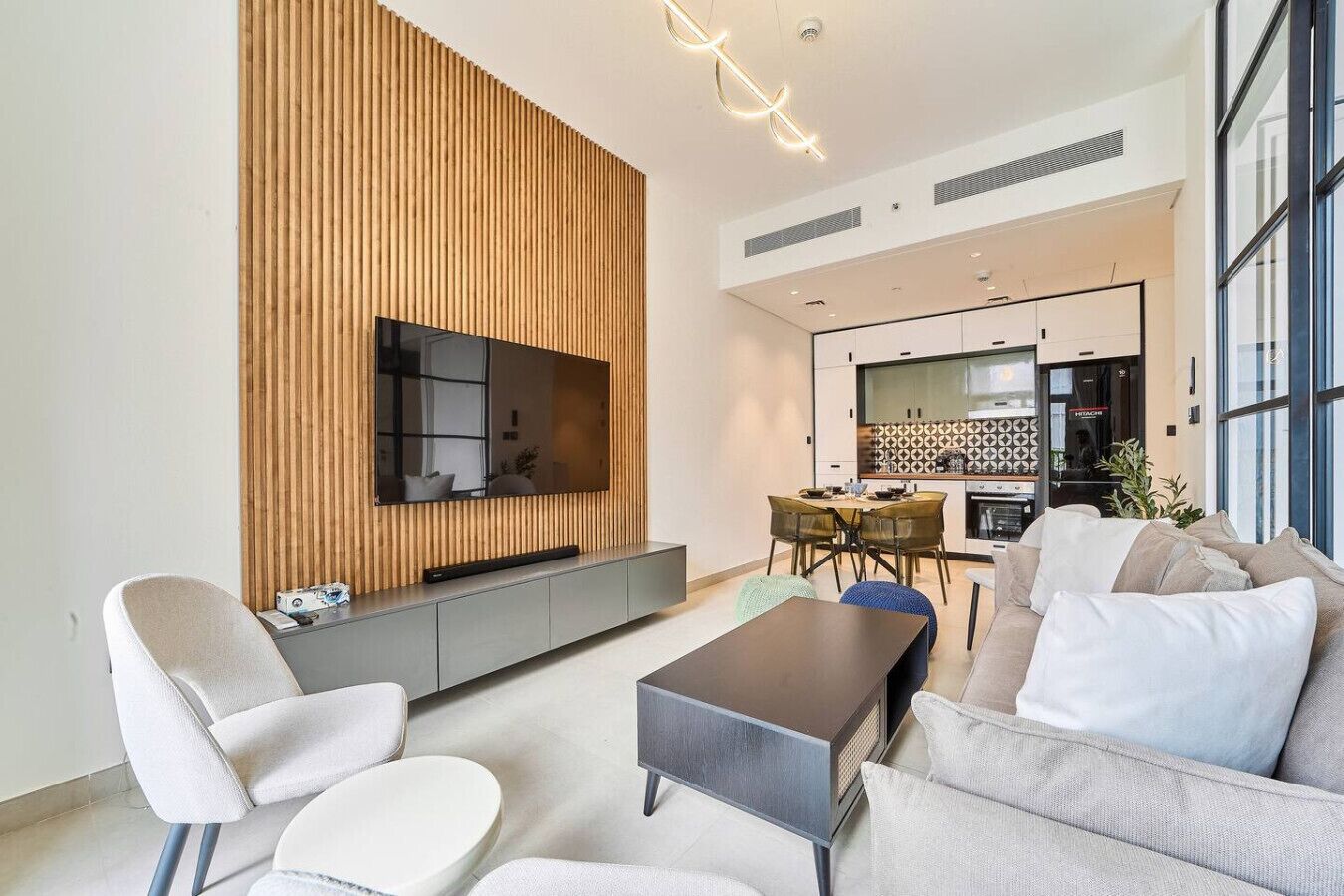 A modern living room with a flat-screen TV, a wooden accent wall, a dining area, and a sofa.