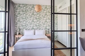 Un dormitorio moderno con una cama grande, una mesita de noche, una lámpara y vistas a través de un ventanal.