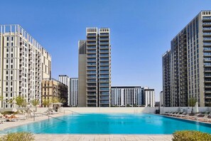 Un complejo residencial moderno con piscina central, varios balcones y un cielo azul despejado.