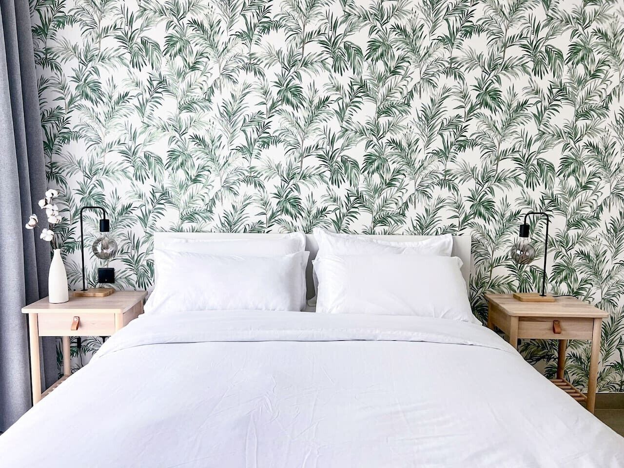 A bedroom with a bed, two nightstands, a lamp, and a wall with a tropical leaf pattern.