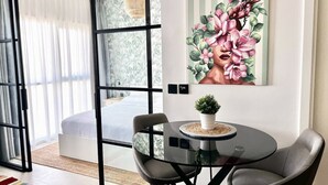 A modern room with a glass door leading to a balcony, a round glass table with chairs, and a floral painting on the wall.
