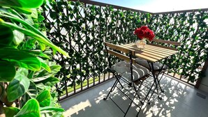 A balcony with a wooden table and chairs, surrounded by lush green plants and a decorative metal fence.