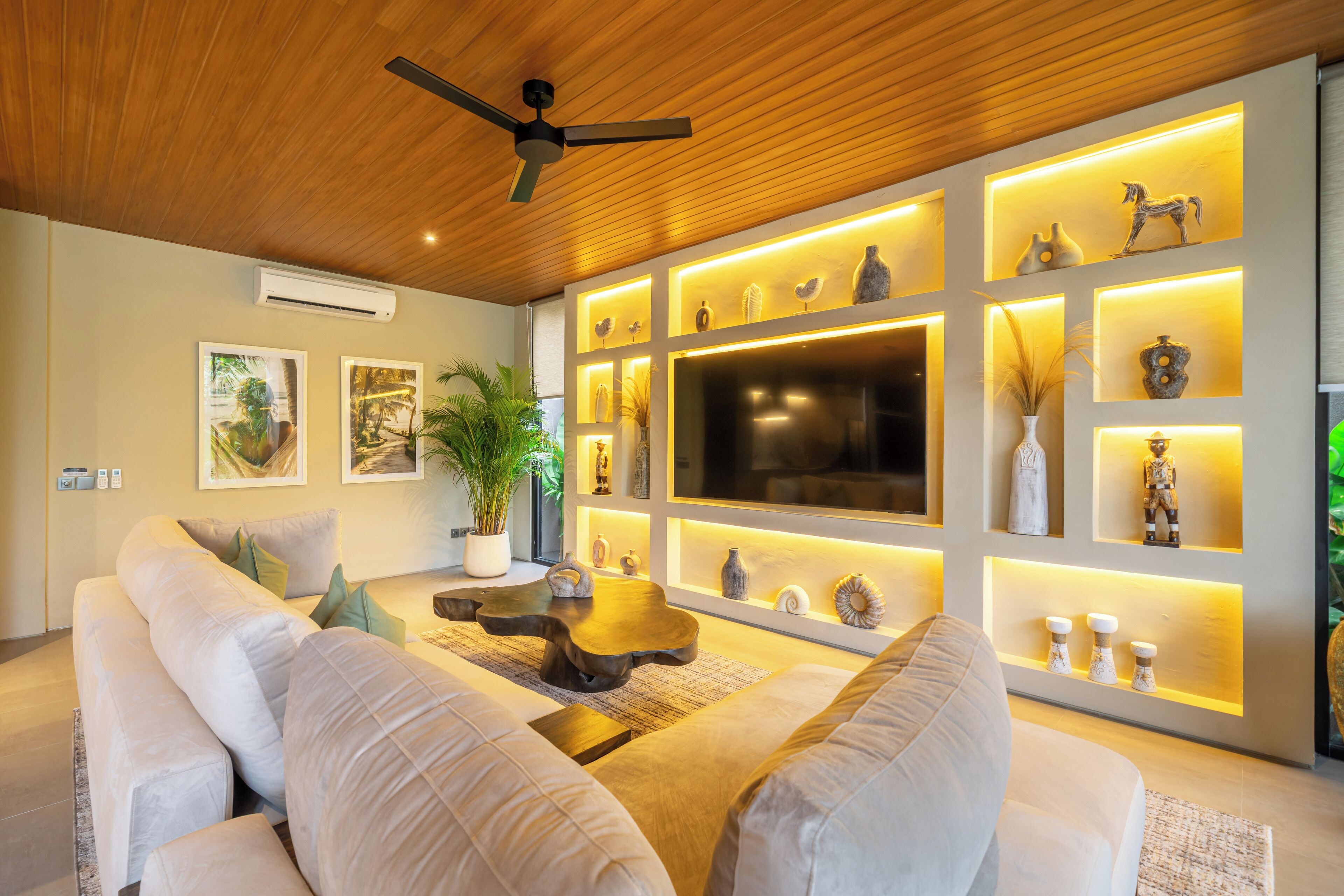 A modern living room with a wooden ceiling, a flat-screen TV, and a wall-mounted shelf with decorative items.