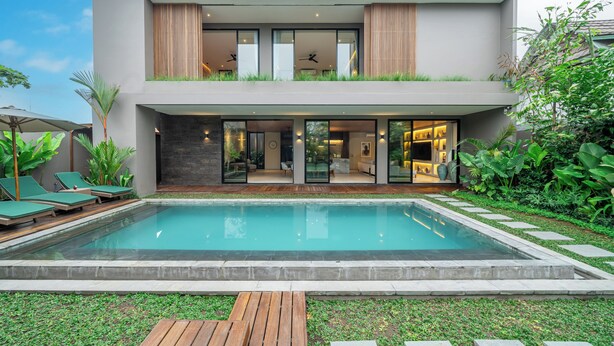 Uma casa moderna de dois andares com piscina, área de estar externa e vegetação exuberante.