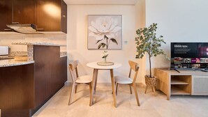 Een moderne keuken met donkerhouten kastjes, een granieten aanrecht en een eethoek met twee stoelen en een kleine tafel. Aan de muur hangt een groot bloemenportret en staat een potplant.