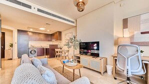 Een moderne woonkamer met een bank, een salontafel en een televisie. In de achtergrond bevindt zich een keuken met een wasmachine.