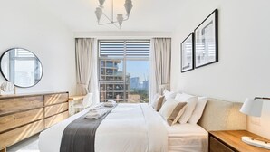 Une chambre d’hôtel moderne avec un grand lit, une commode en bois, une table de chevet et une vue sur le paysage urbain par la fenêtre.