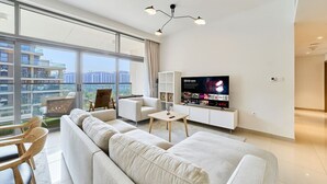 Un salon moderne doté d’un grand téléviseur, d’un canapé, d’une table basse et d’un balcon offrant une vue sur la ville.