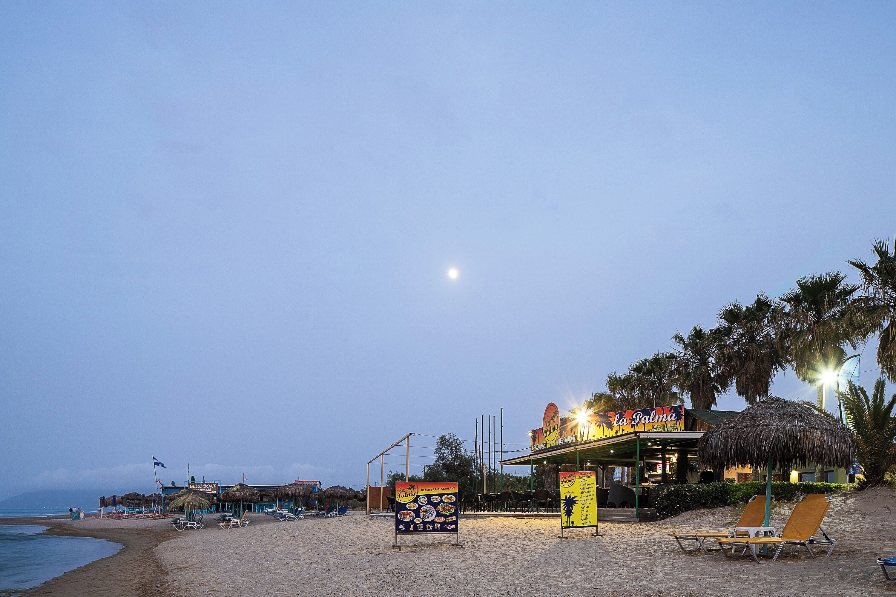 A beachside restaurant with outdoor seating and a thatched roof.