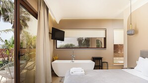 A modern hotel room with a large bed, a bathtub, a TV, and a balcony with plants. - La Palma Beachfront Suites (Apokoronas)
