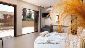 A modern hotel room with a large bed, a flat-screen TV, and a balcony with a view of greenery. - La Palma Beachfront Suites (Apokoronas)