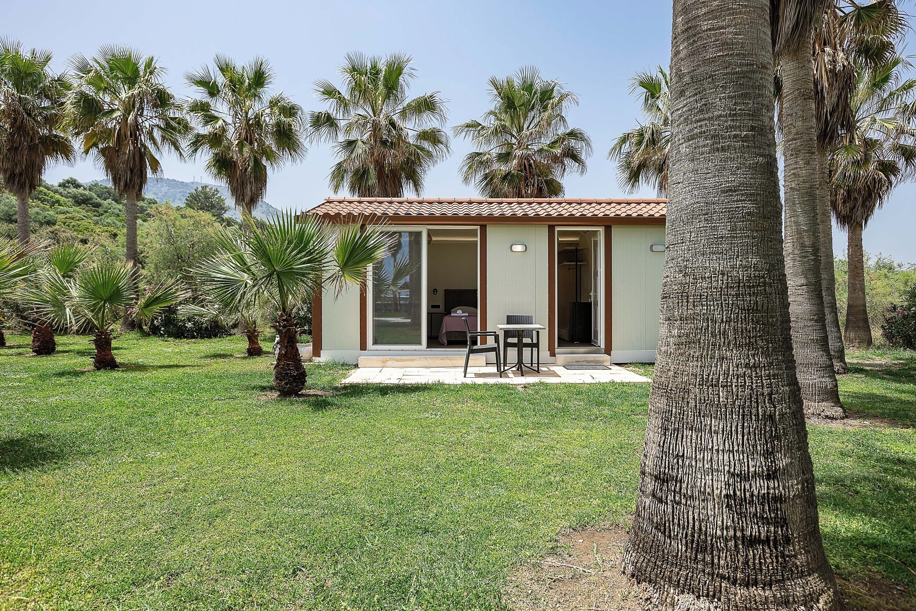 A small house with a tiled roof, surrounded by palm trees and a grassy lawn.