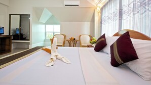 A hotel room with a neatly made bed, a desk with a computer, and a seating area with chairs and a small table. - Damnak Riverside Villa (Siem Reap)