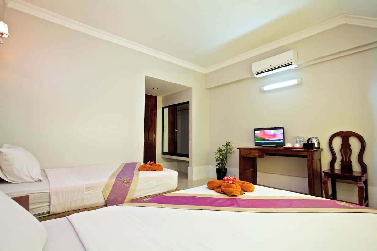 A hotel room with two beds, a desk with a television, and an air conditioning unit.