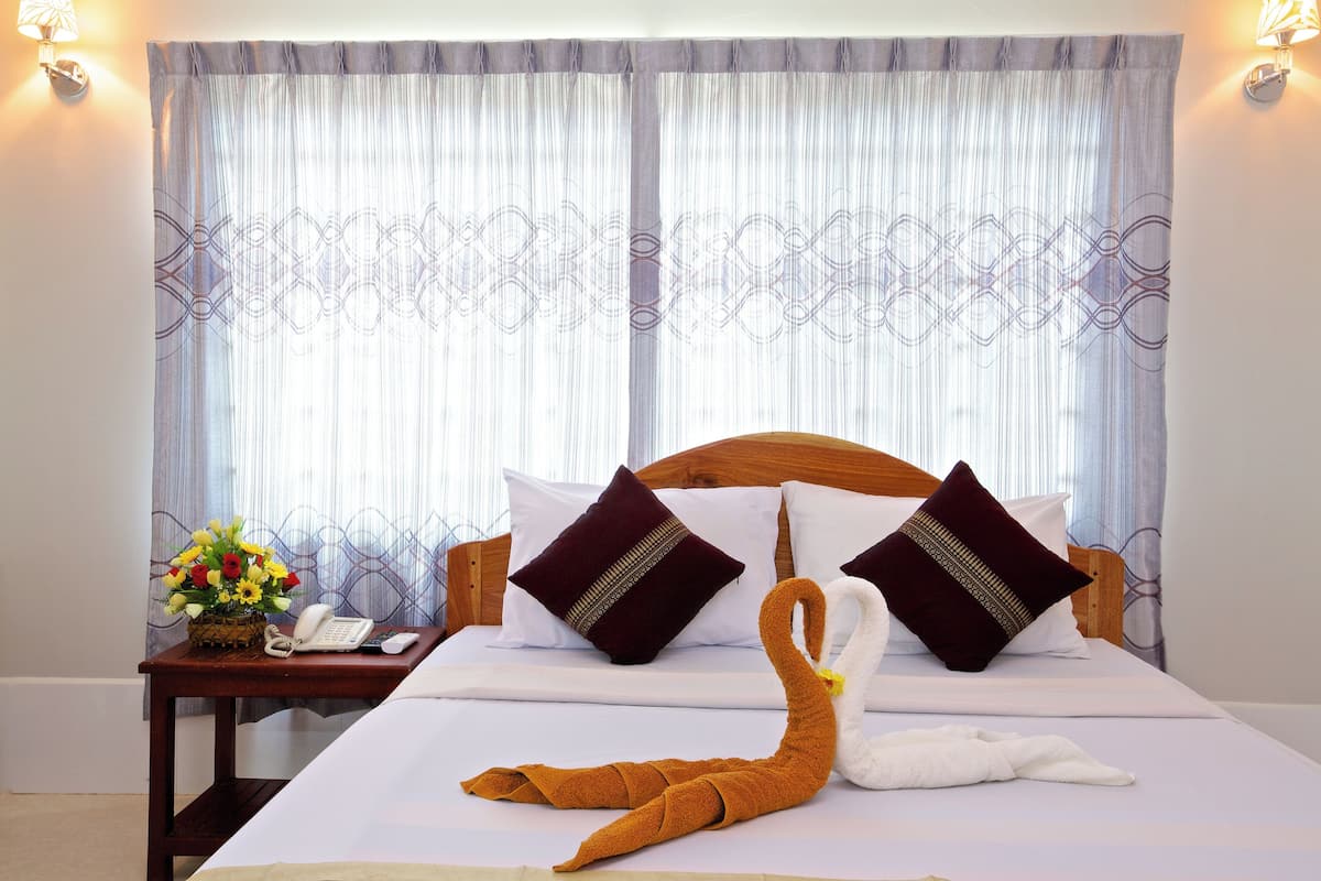 A hotel room with a neatly made bed, a wooden headboard, and a nightstand with a phone and a vase of flowers.