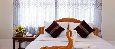 A hotel room with a neatly made bed, a wooden headboard, and a nightstand with a phone and a vase of flowers.