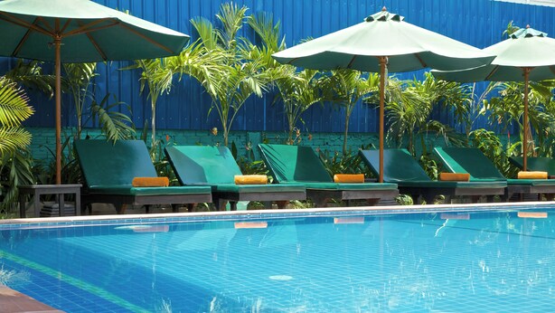 A swimming pool with green lounge chairs and umbrellas, surrounded by palm trees. - Damnak Riverside Villa (Siem Reap)
