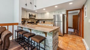 A modern kitchen with a central island, bar stools, stainless steel appliances, and a wooden ceiling. - HotTub, Grill | Main St-Shops, Lake (Frisco)
