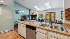 A modern kitchen with a dishwasher, granite countertops, and a large window offering a view of the outdoors. - HotTub, Grill | Main St-Shops, Lake (Frisco)