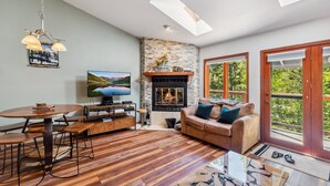 A modern living room with a fireplace, wooden flooring, a round dining table, a sofa, and a TV. - HotTub, Grill | Main St-Shops, Lake (Frisco)