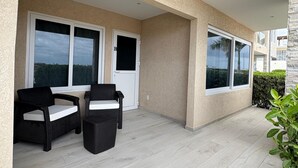 A covered outdoor area with two wicker chairs and a table, a door labeled 'B', and large windows. - Sunset Bliss Suite at Commandeurs (Oranjestad)