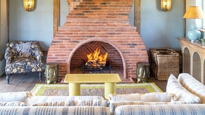 A rustic interior with exposed wooden beams, a brick fireplace, and a patterned armchair.