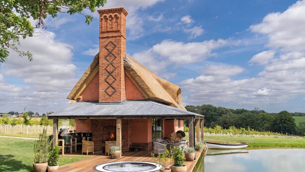 A rustic house with a chimney, a hot tub, and a boat on a pond.