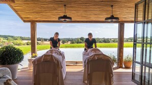 A wooden deck with two massage tables, a potted plant, and a view of a lake.