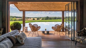A room with a wooden deck, two wicker chairs, a small table, and a sofa with cushions.