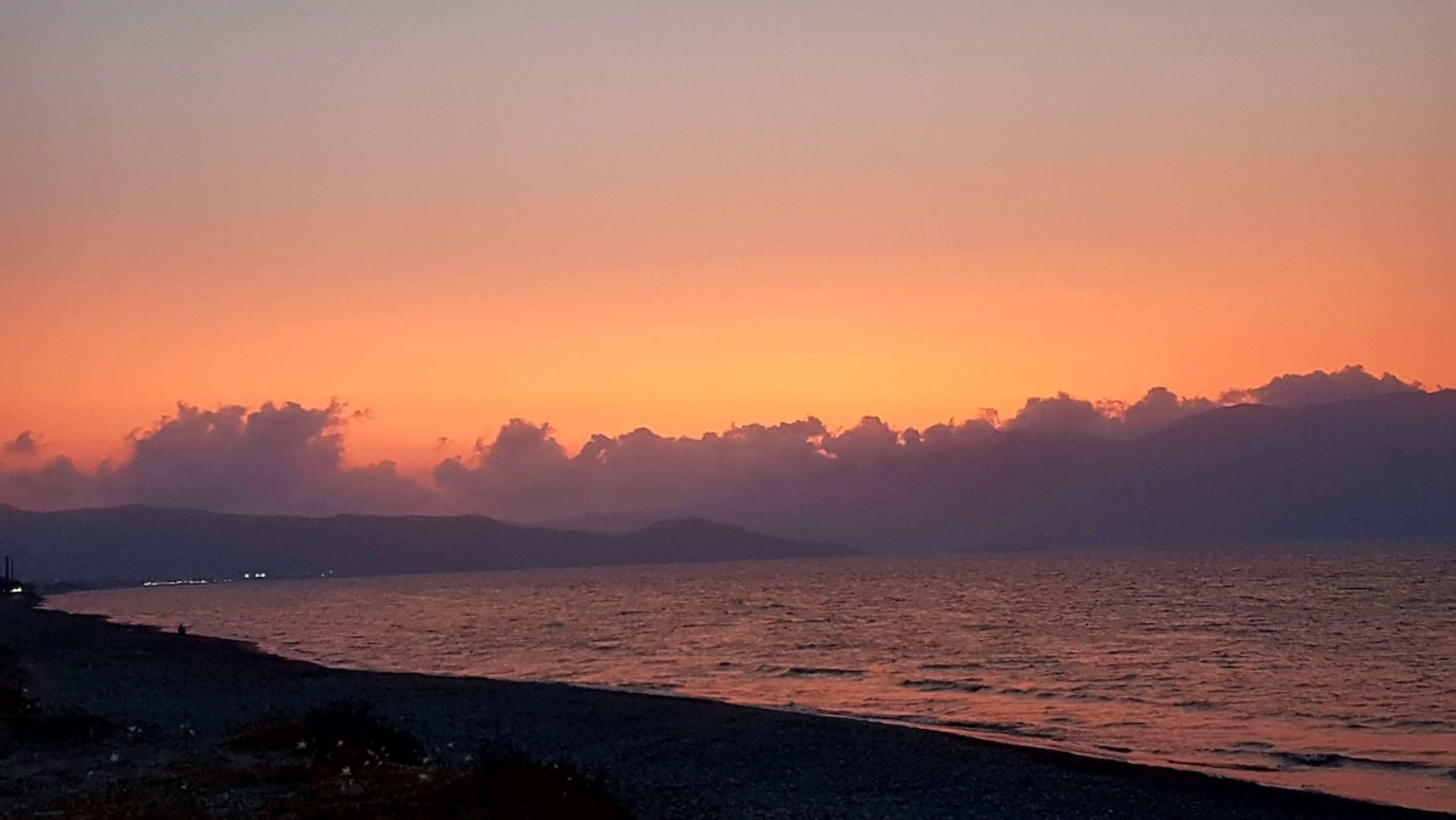 A sunset over a calm sea with a distant shoreline.