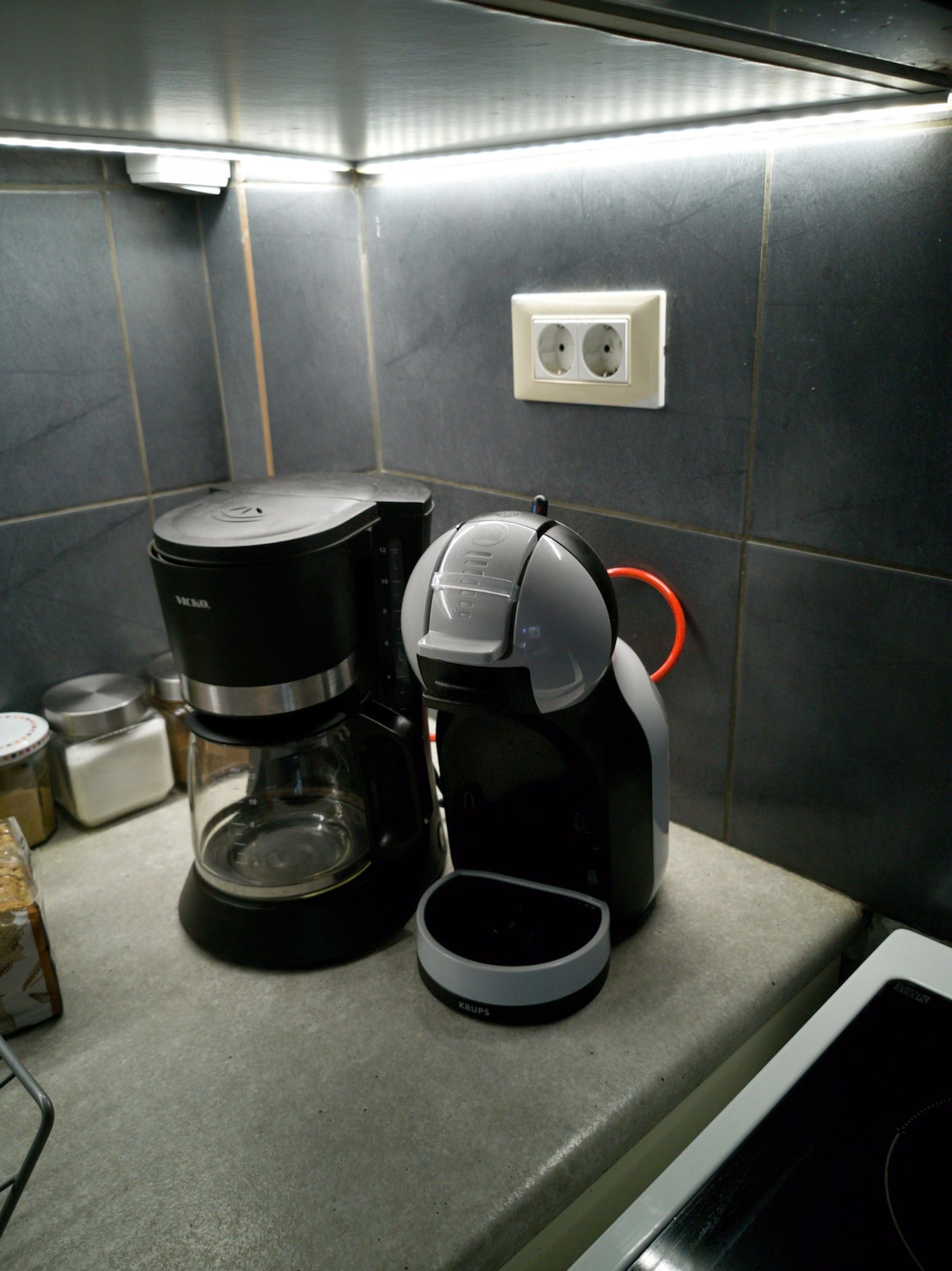 Una cocina con una cafetera, un hervidor y una jarra de café sobre la encimera.