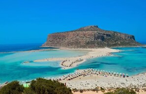 Ein Küstenstrand mit klarem türkisblauem Wasser, einem Sandufer und einem markanten Felsen im Hintergrund.