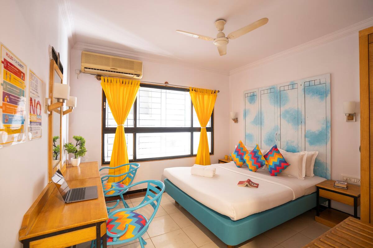 A bedroom with a bed, a desk, a chair, a ceiling fan, and a window with curtains.