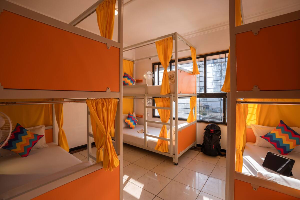 A dormitory room with bunk beds, a fan, and a window with curtains.