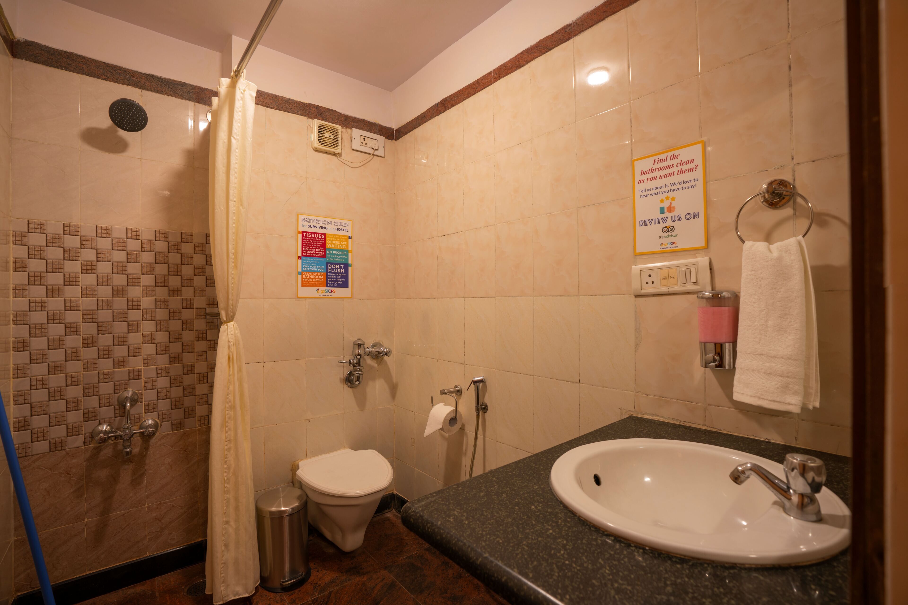 Une salle de bain équipée d’une douche, de toilettes, d’un lavabo et d’un sèche-mains. Des panneaux affichés sur le mur indiquent les règles à respecter dans la salle de bain.
