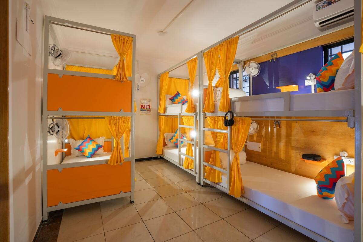 A dormitory room with bunk beds, orange curtains, a fan, and a 'NO' sign on the wall.
