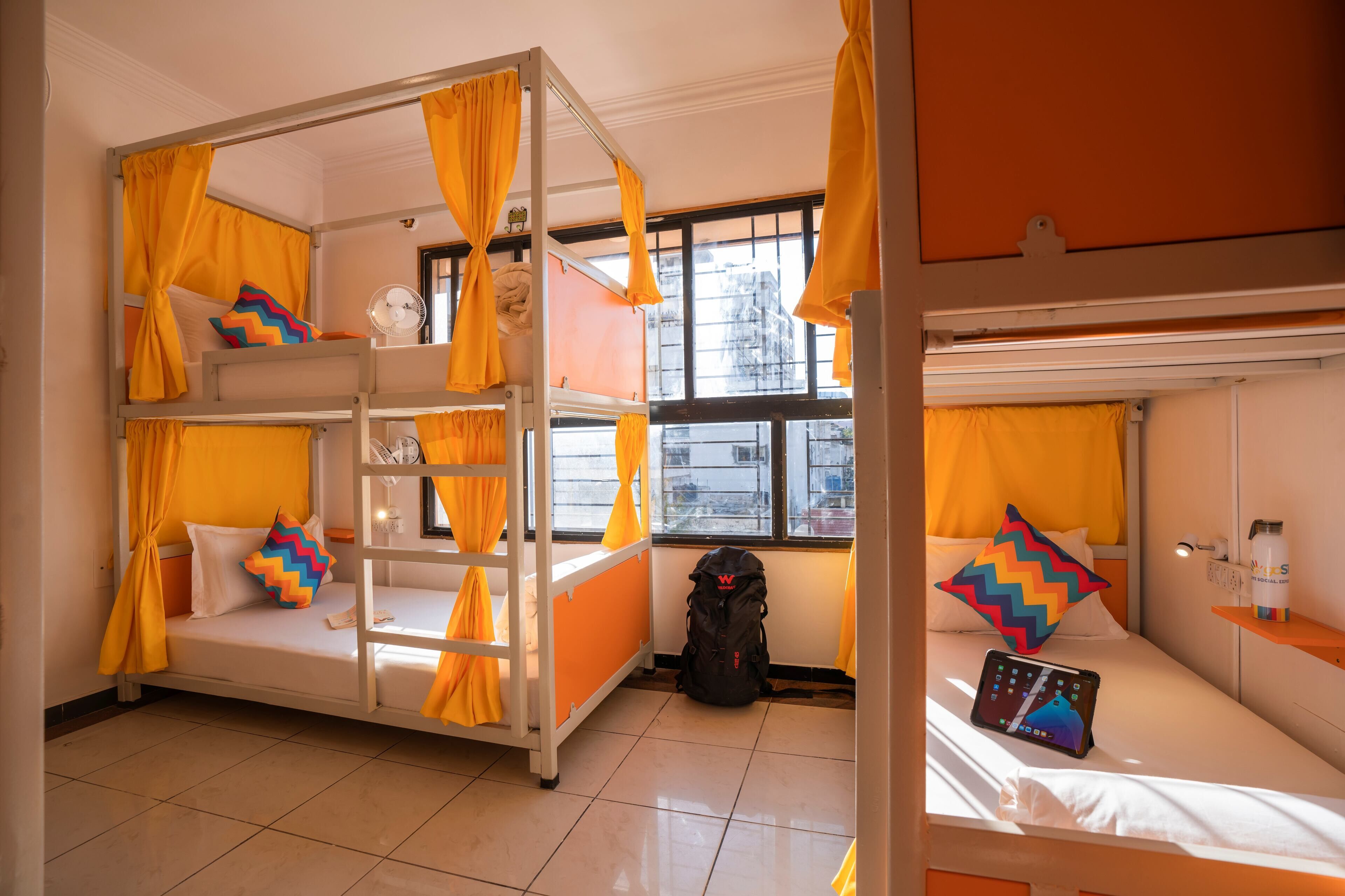 A bunk bed room with yellow curtains, a backpack, and a tablet on the bed.