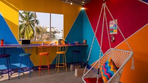 A vibrant room with colorful walls, a hanging chair with a colorful cushion, and a bar area with stools and a laptop. - goSTOPS Bengaluru Gandhi Nagar Majestic. (Bengaluru)
