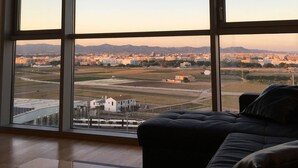 A room with a large window, a hanging lamp, a sofa, and a view of a cityscape.