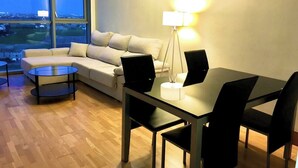 A modern living room with a sofa, a glass coffee table, a dining table with chairs, and a floor lamp.