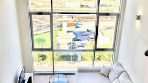 A modern living room with a large window, a sectional sofa, a glass coffee table, and a small side table.