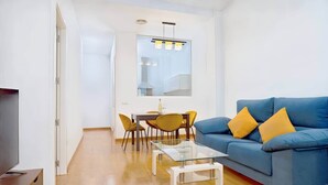 Un salon moderne avec un canapé bleu, des coussins jaunes, une table basse en verre et un coin repas avec des chaises jaunes.