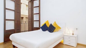 Une chambre avec un grand lit, une table de chevet avec une lampe et une vue à travers une porte en bois.